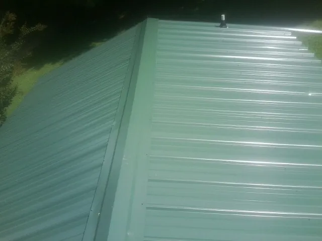 New green metal panels meeting at the ridge of a roof — Flat Roof Repair work by our crew in Dewitt