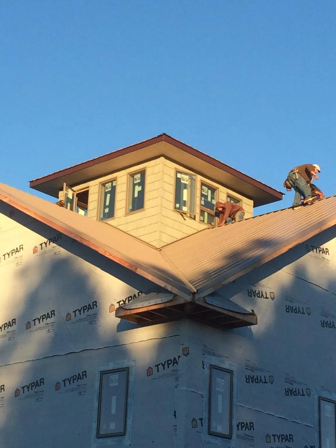 Roofers working around a rooftop cupola on a new metal roof at sunset — Roof Waterproofing in Dewitt by Roofing Brothers